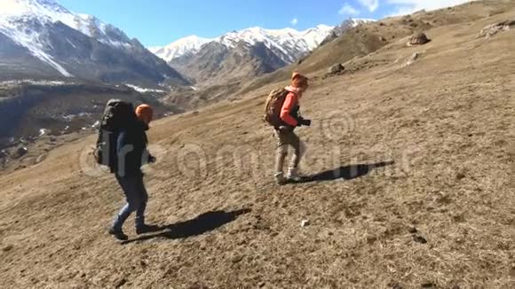 两个戴着帽子和太阳镜背包的游客摄影师带着相机在黄草上山视频的预览图