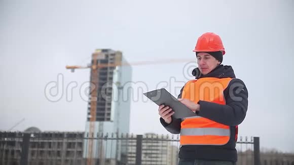 建筑设计师戴着头盔和橙色背心的工人背景是一台多层冬季起重机视频的预览图