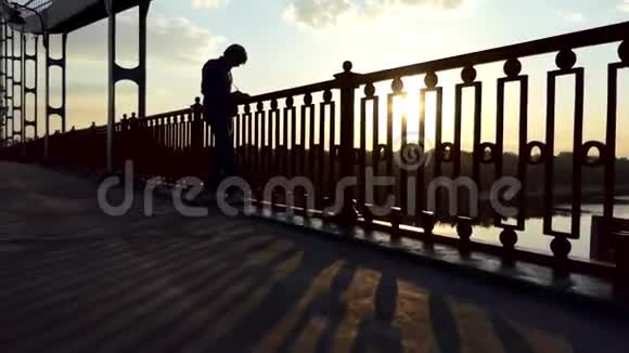 年轻人站在夕阳下的河桥上写下自己的想法视频的预览图