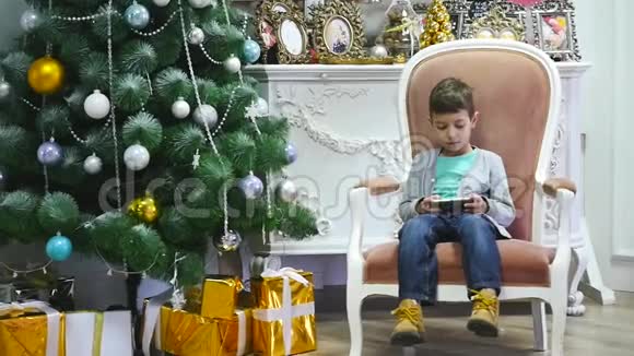 男孩在圣诞树附近玩手机儿童和智能手机视频的预览图