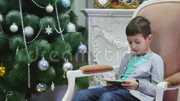男孩在圣诞树附近玩手机儿童和智能手机视频的预览图