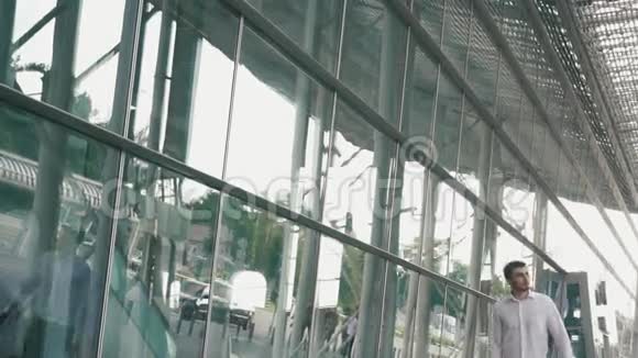 英俊的商人戴着眼镜和手提箱在现代机场航站楼玻璃墙背景旅行者视频的预览图