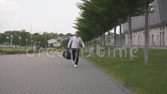 外观英俊优雅的商人穿着白色衬衫带着大行李箱慢动作跑城市背景视频的预览图