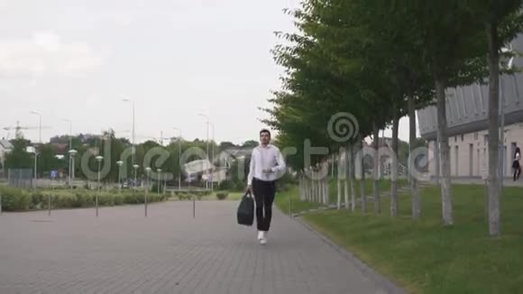 英俊的商人带着胡子跑着带着一个大手提箱在慢动作中的正面景色城市背景视频的预览图