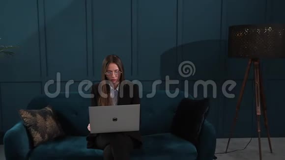 一位优雅的女商人坐在豪华蓝色办公室内部的沙发上手提电脑的肖像视频的预览图
