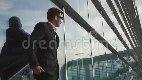 漂亮的年轻商人戴着眼镜等着他的航班玻璃机场墙背景视频的预览图