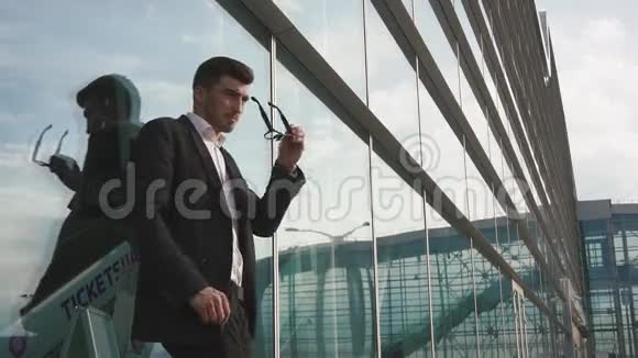 一位戴着眼镜的英俊紧张的商人在等他弱智的飞行玻璃机场墙背景视频的预览图