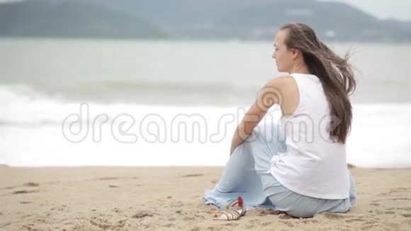 年轻的女人坐在海滩上天气不好看着大海视频的预览图