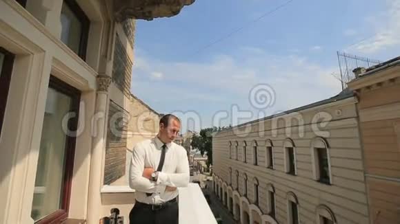 年轻英俊的商人站在阳台上在他的手表上检查时间视频的预览图