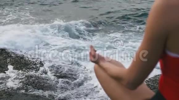 平静的女人在暴风雨的海洋前的岩石海滩上练习瑜伽健身运动视频的预览图