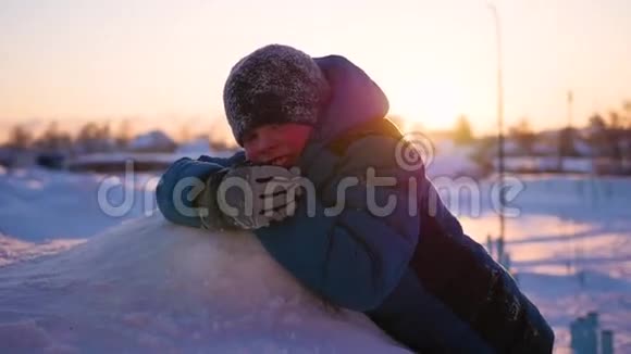 孩子躺在雪地上看着日落冬季公园视频的预览图