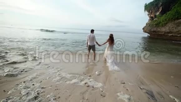 新婚夫妇在傍晚或日落时在海边散步牵手拥抱在海洋附近浪漫视频的预览图