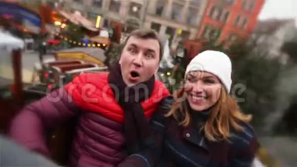 夫妇在圣诞集市上笑着玩冬假期间的朋友在旋转木马或欢乐之旅视频的预览图