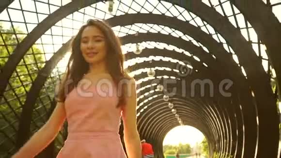 美丽的黑发女孩穿着粉红色的连衣裙走过拱形通道慢动作安定夹视频的预览图