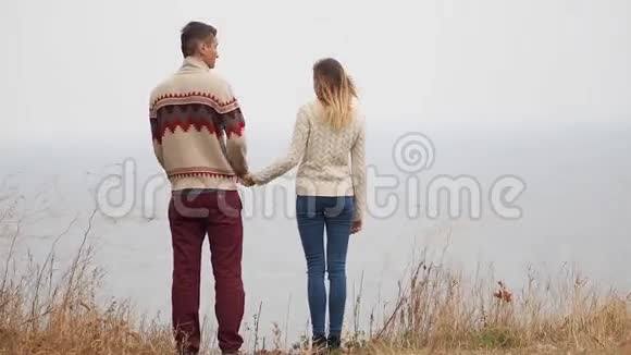 一对年轻迷人的夫妇穿着针织毛衣在海边的悬崖上取笑拥抱和亲吻视频的预览图