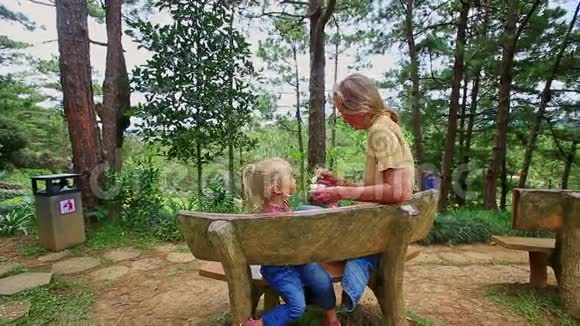 在公园的木凳上妈妈用勺子喂小女孩视频的预览图