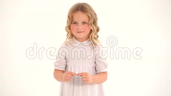 可爱的小害羞的小可爱的小女孩蹒跚学步的孩子金色的卷发穿着白色的连衣裙用手指在空中画出一颗大大的心视频的预览图