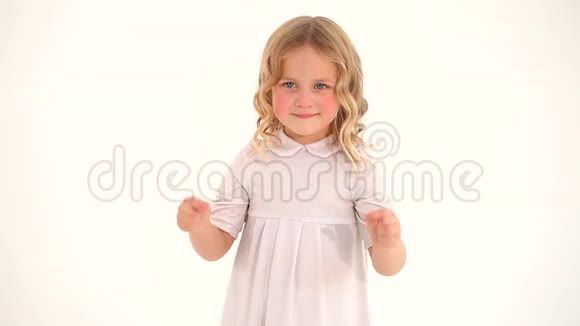 可爱的小害羞的小可爱的蹒跚学步的女孩一头金发穿着白色连衣裙用手指在空中画着一颗大大的心视频的预览图