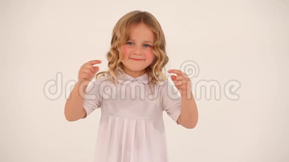 可爱的小可爱的小女孩蹒跚学步的孩子一头金色卷发穿着白色连衣裙用手指在空中画出一颗大大的心视频的预览图