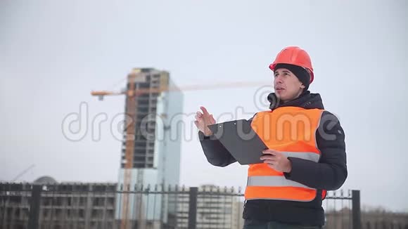 建筑设计师戴着头盔和橙色背心的工人背景是一栋多层房屋冬季起重机视频的预览图