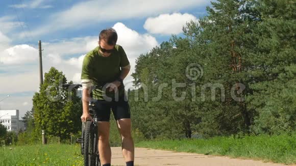 骑自行车的人检查自行车轮子穿着自行车短裤和太阳镜的年轻人慢动作视频的预览图