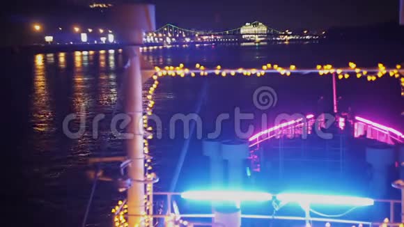照亮的假日小船沿着夜晚的城市灯光漂浮在河上视频的预览图