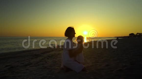 日落时分年轻漂亮的女人和她的小女儿在海滨散步妈妈把女儿抱在怀里他们视频的预览图