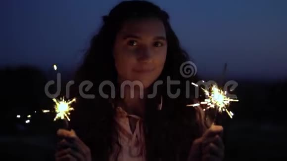 年轻女孩手里拿着烟花在一个夜城的背景上慢动作视频的预览图