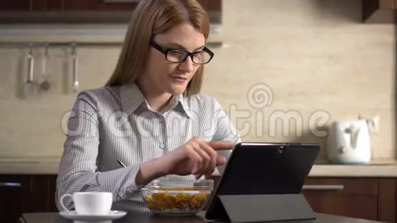 美丽的年轻迷人的女商人早餐吃玉米片并使用她的平板电脑视频的预览图