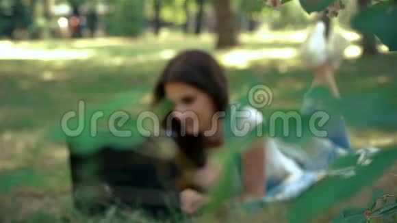 可爱的黑发女人手提电脑躺在绿草上视频的预览图