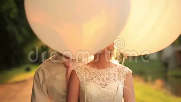 在秋天的公园里一对年轻的新婚夫妇带着气球做着滑稽的脸在夕阳的背景下笑着视频的预览图