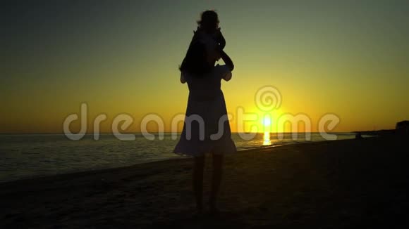 日落时分年轻漂亮的女人和她的小女儿在海滨散步妈妈把女儿抱在怀里他们视频的预览图