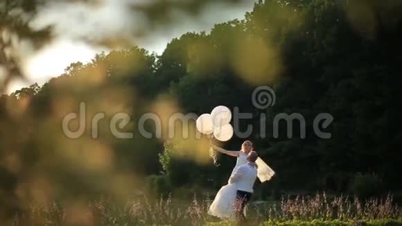 性感的爱情时刻快乐的新郎手里拿着漂亮的金发新娘和气球阳光夏日田野背景视频的预览图