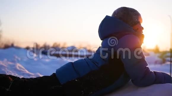 孩子躺在雪地上看着日落冬季公园视频的预览图