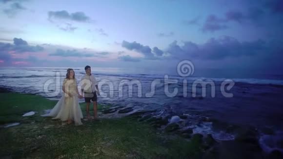 新婚夫妇在傍晚或日落时在海边散步牵手拥抱在海洋附近浪漫视频的预览图