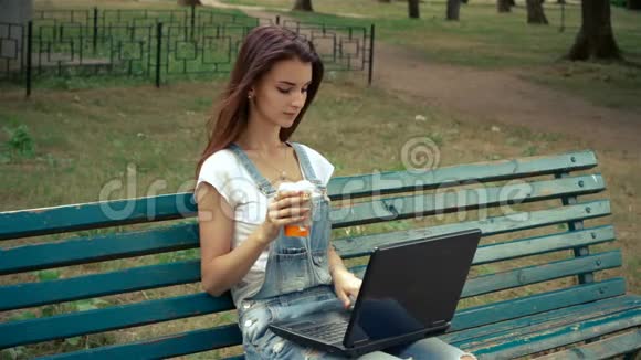 一位迷人的黑发少女坐在公园里手提电脑视频的预览图