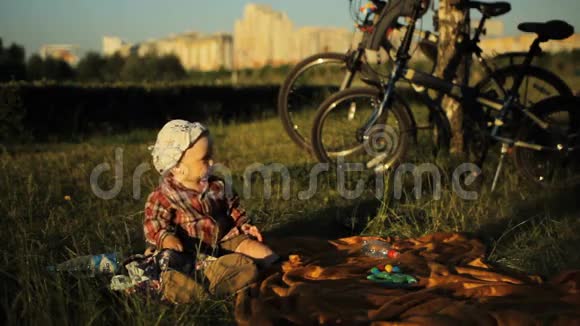 夏天日落时分戴着帽子的可爱小男孩坐在公园里一个孩子摘下帽子视频的预览图