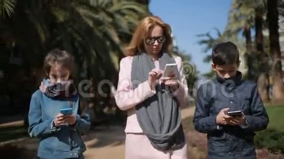 有孩子的女人妈妈和孩子们沿着小巷走着每个人都在忙着打电话视频的预览图