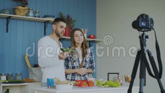 一对迷人的情侣在家里用dslr摄像机录制关于烹饪的视频食物博客视频的预览图