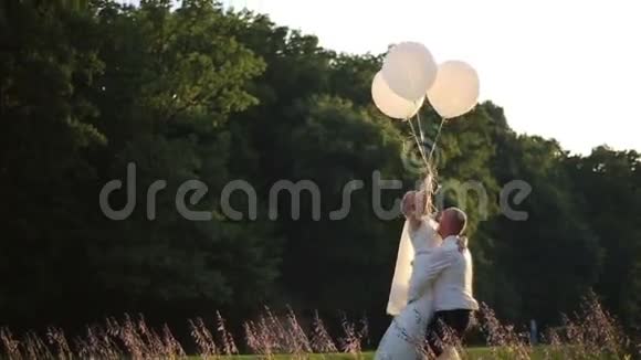 性感的爱情时刻快乐的新郎手里拿着气球的新娘阳光夏日田野背景视频的预览图