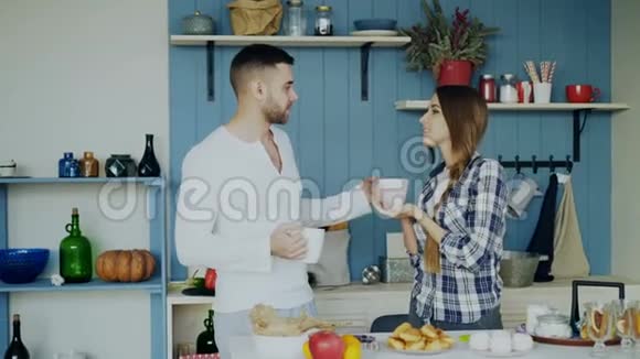 一对漂亮的夫妇早上在家里的厨房里聊天喝咖啡视频的预览图