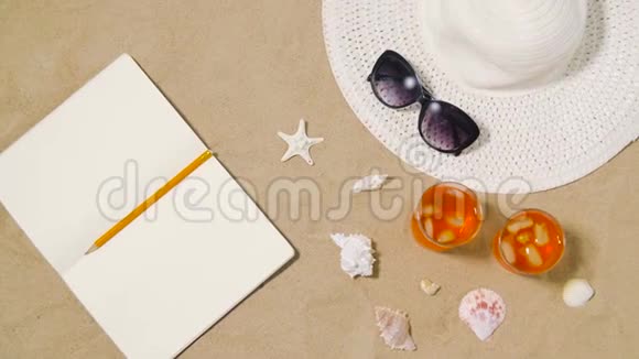 沙滩沙上的笔记本鸡尾酒帽子和墨镜视频的预览图