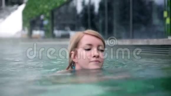 穿着蓝色比基尼的年轻女人远离相机在户外游泳池里尽情享受视频的预览图