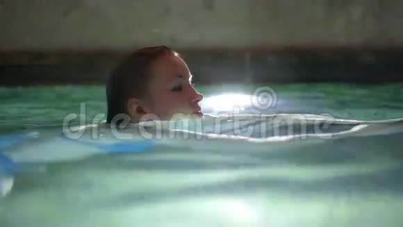 穿着蓝色比基尼的年轻女子在室内游泳池游泳和享受视频的预览图