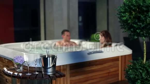 年轻夫妇在按摩浴缸里放松前面有香槟和糖果视频的预览图