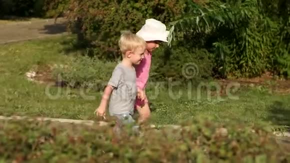 两个可爱的孩子在夏天公园的小巷里散步视频的预览图