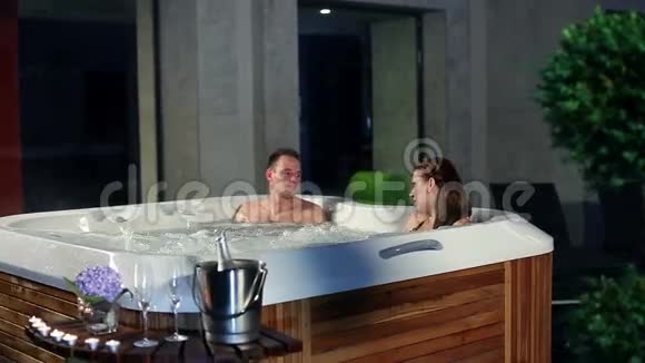 年轻夫妇在按摩浴缸里放松前面有香槟和糖果视频的预览图