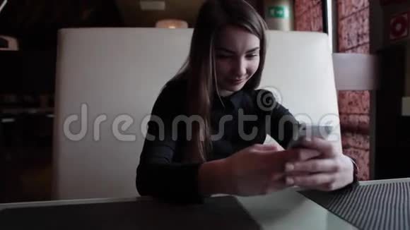 智能手机女孩在手机上使用应用程序在咖啡馆里微笑地喝咖啡视频的预览图