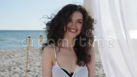 在海边度过暑假的女性美丽的脸上带着微笑沙滩上有白色窗帘的平房快乐视频的预览图