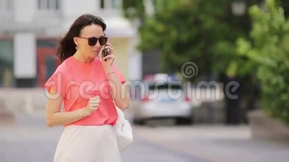 年轻的白种人女孩在她的智能手机户外交谈戴墨镜的漂亮女孩在街上使用智能手机和视频的预览图